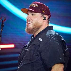 Luke Combs holding his hands up in the air on-stage