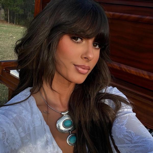 Ella Langley taking a selfie photo outside wearing a white top standing in front of a brown piano.