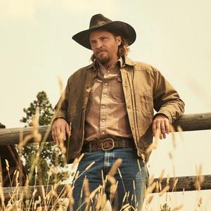 Luke Grimes leaning against a fence in Yellowstone