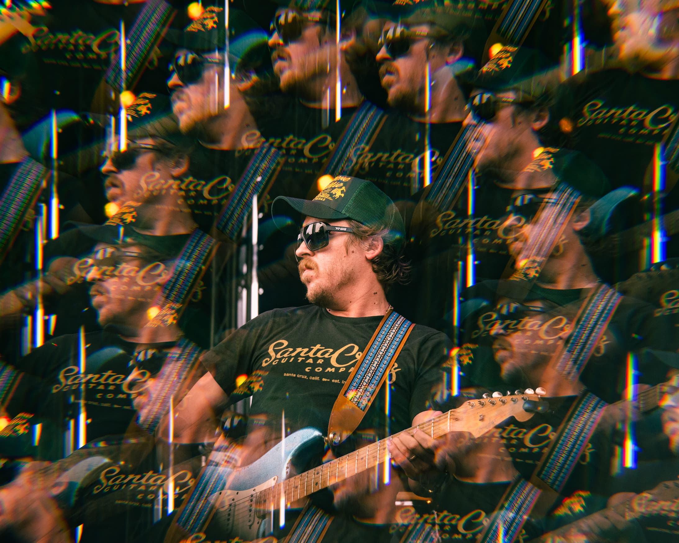 Mike Harmeier of Mike and The Moonpies in sun glasses, cap and Santa Cruz tee looking to the left while playing electric guitar.