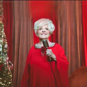 Brenda Lee performing in a red dress aside a Christmas tree