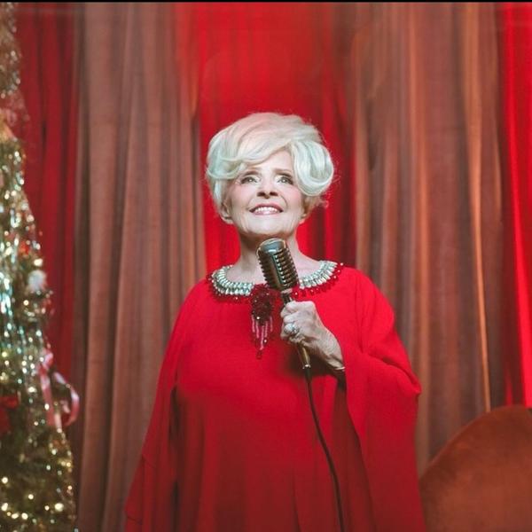 Brenda Lee performing in a red dress aside a Christmas tree