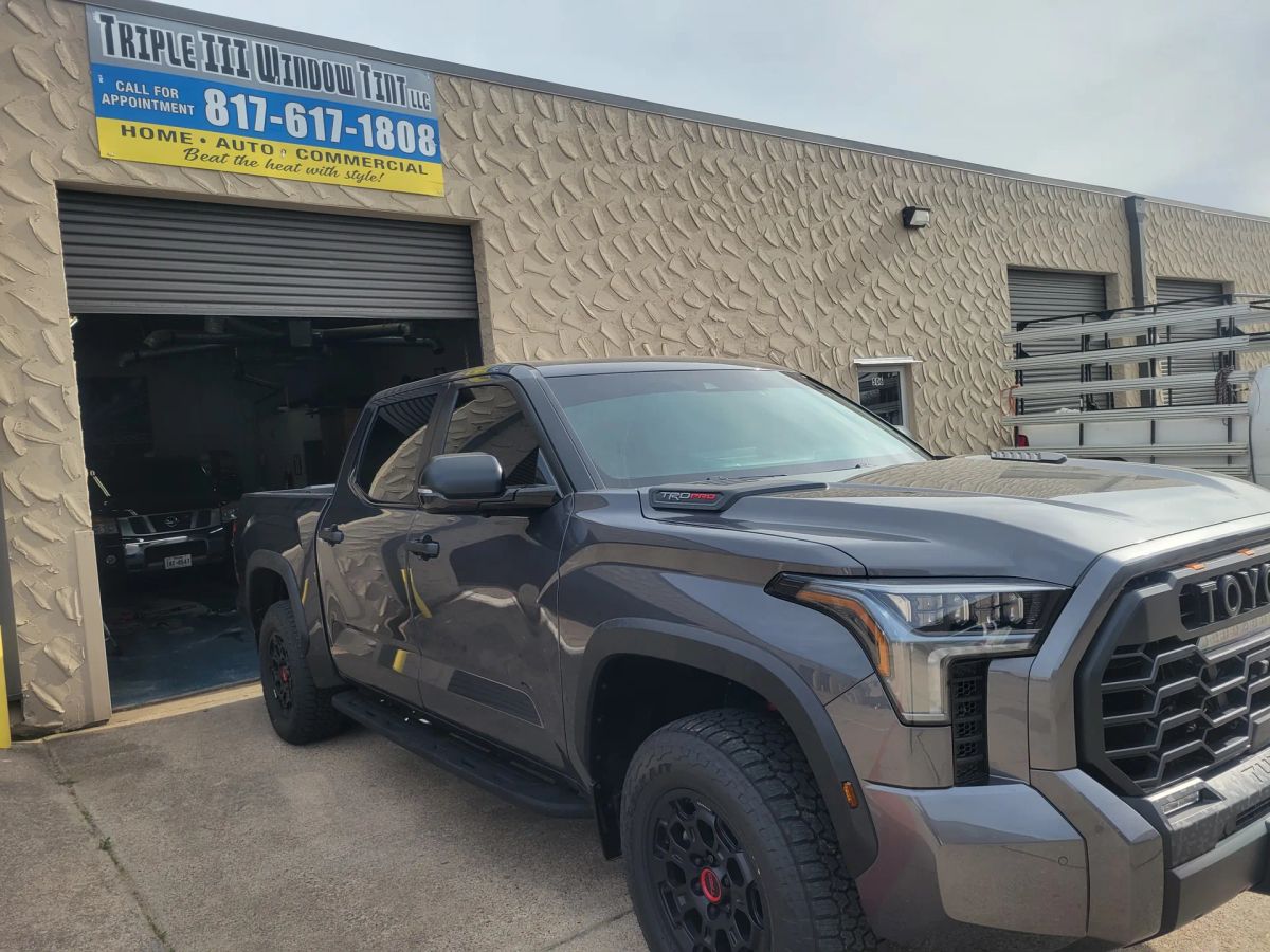 Gray Toyota pickup with dark side-window tint outside the Triple III shop