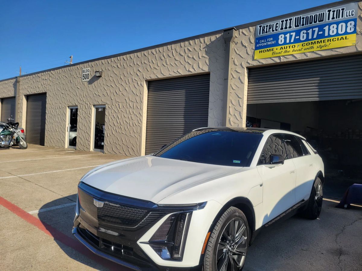 White luxury SUV with dark window tint in front of the Triple III shop