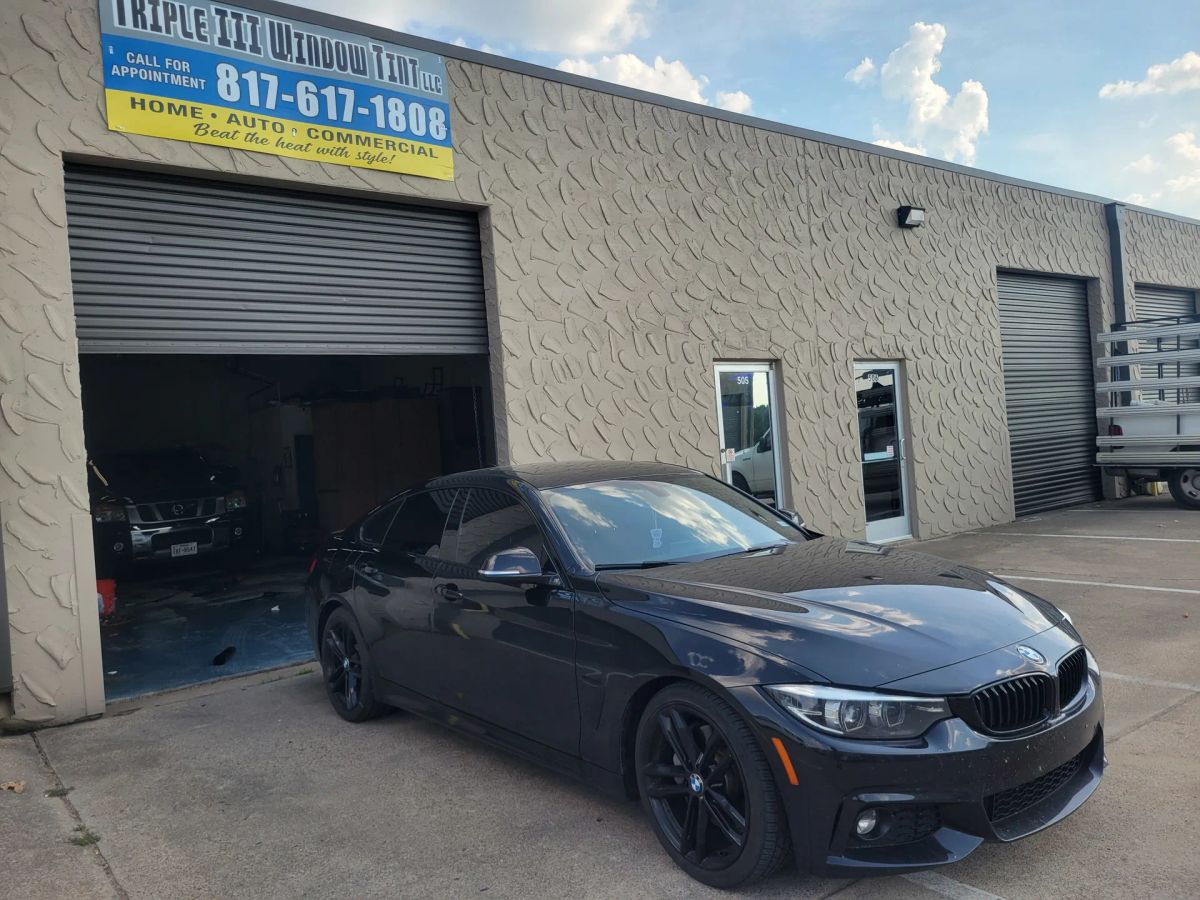Black BMW with dark side-window tint outside the Triple III shop