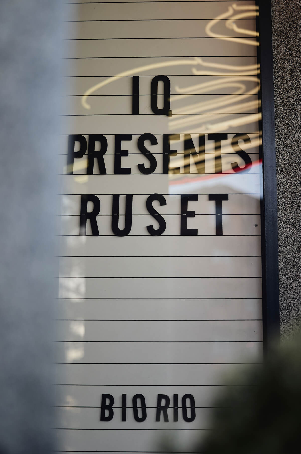 An illuminated cinema directory sign reading "IQ presents Ruset" above Bio Rio, a Stockholm cinema, shot through out-of-focus foliage.