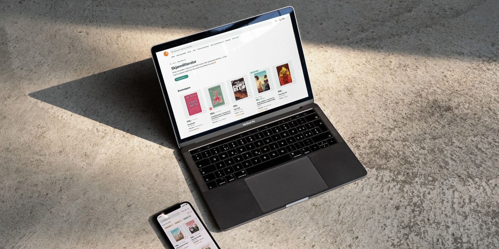 Laptop and smartphone showing an online bookstore, on a concrete surface.