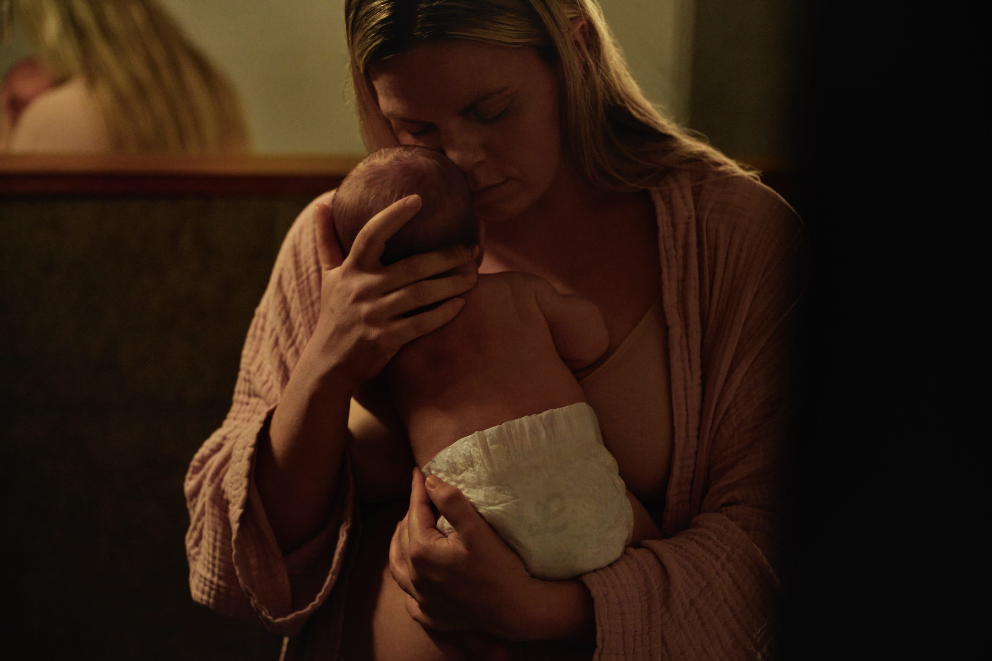 A woman tenderly cradles a baby in dim light.