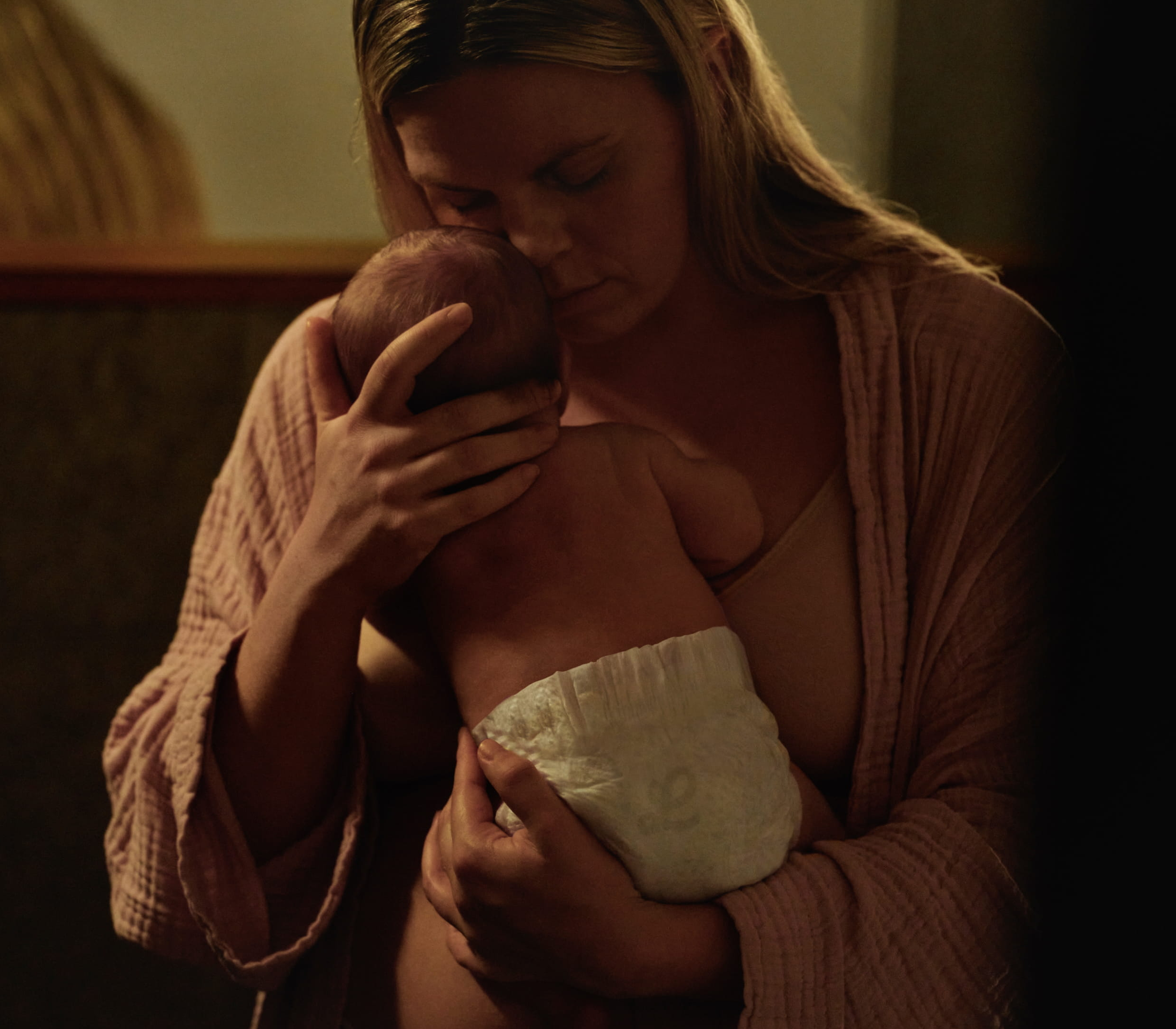 A woman tenderly cradles a baby in dim light.