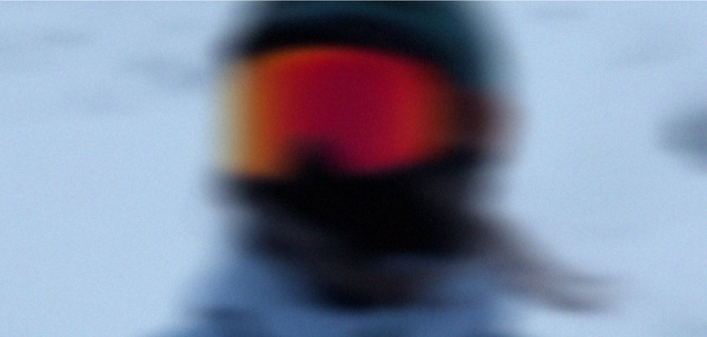 Close-up of a skier's orange-lensed goggles reflecting warm light, face in shadow.
