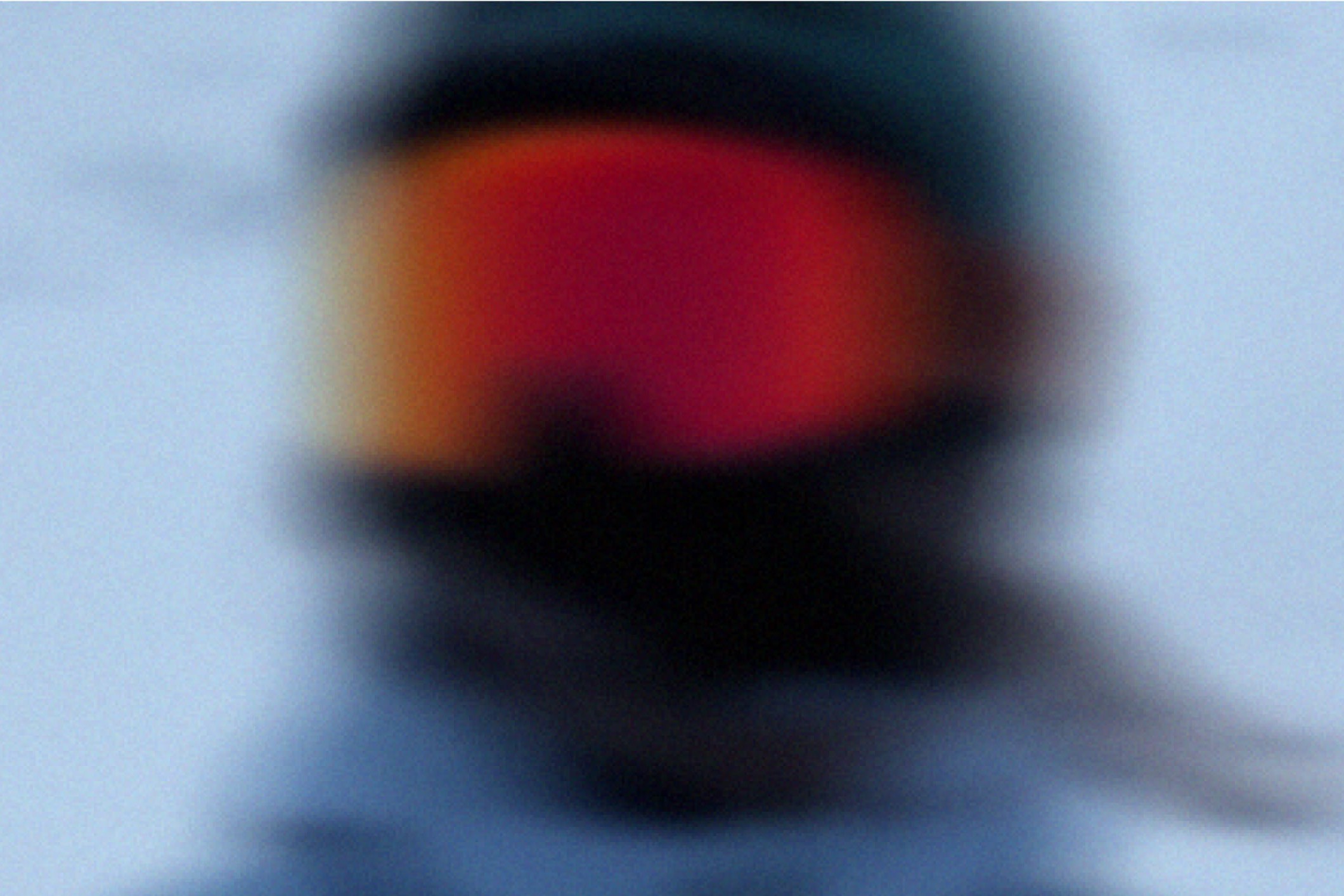 Close-up of a skier's orange-lensed goggles reflecting warm light, face in shadow.