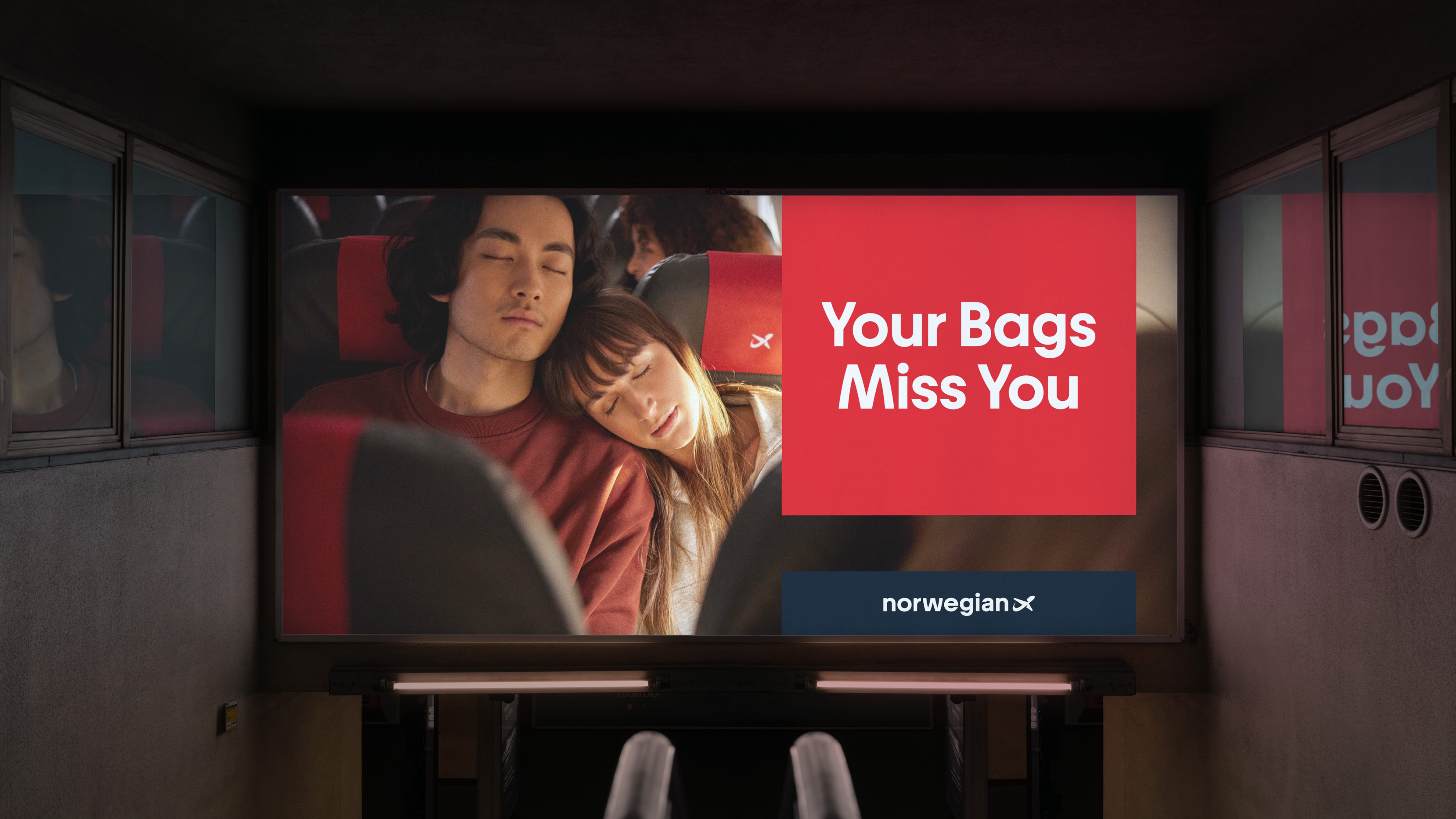 An arrivals hall display showing a couple asleep against each other, beside a red panel reading Your Bags Miss You