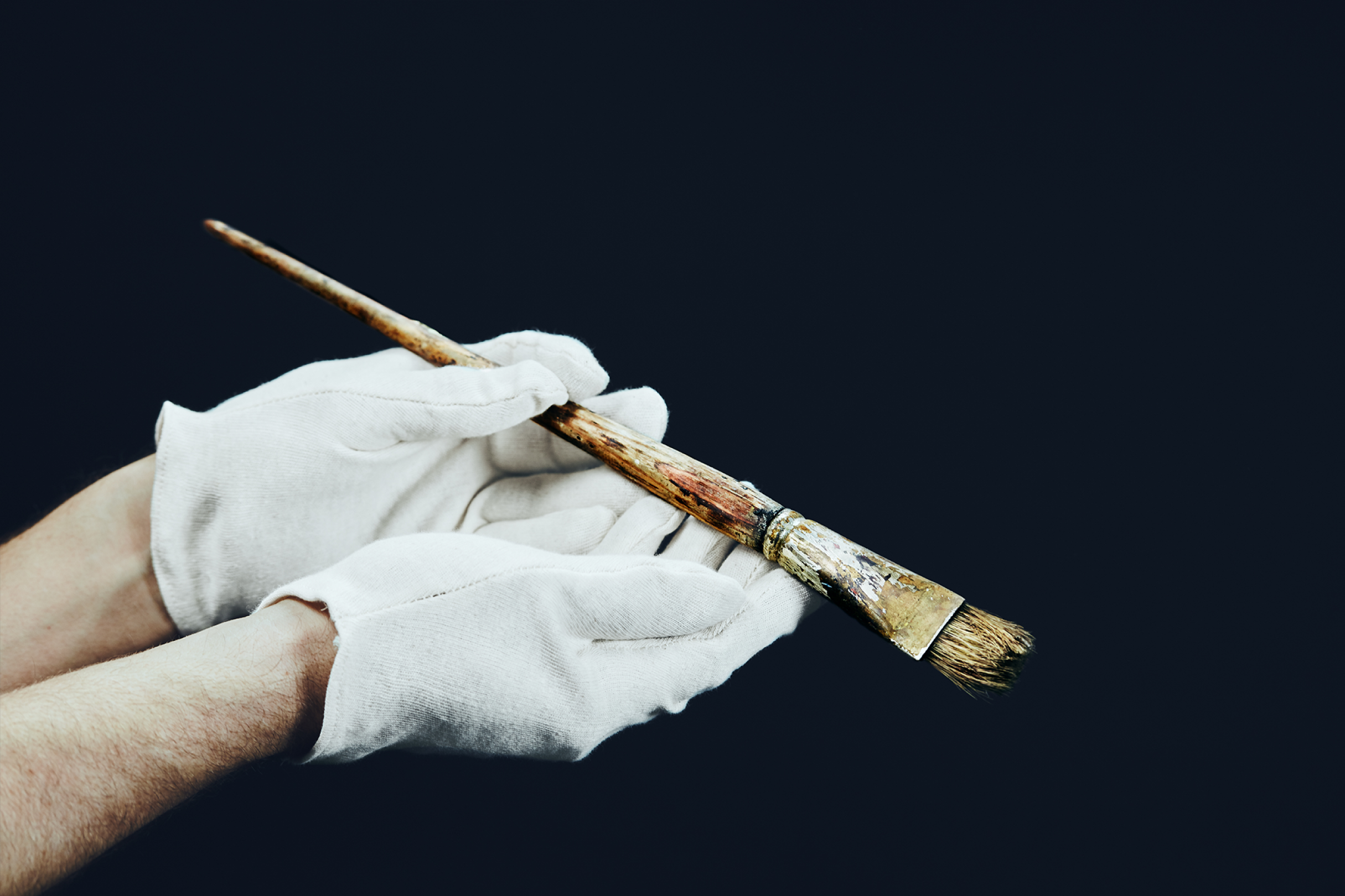 Gloved hands holding a well-worn paintbrush.