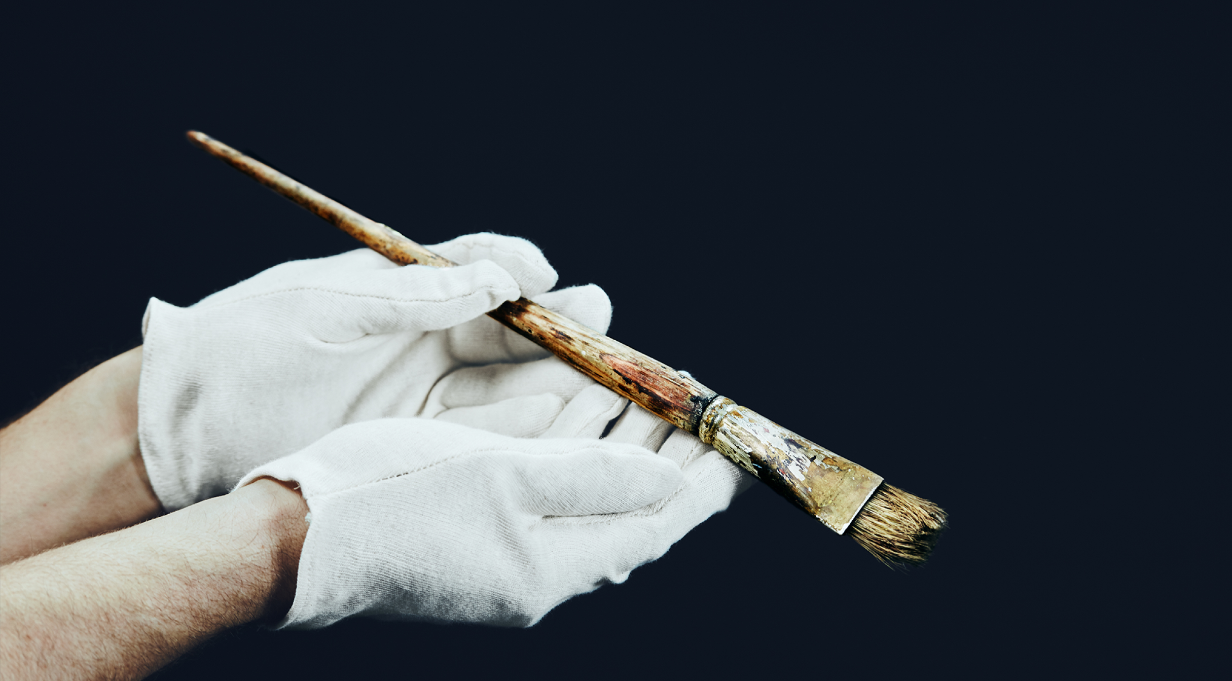 Gloved hands holding a well-worn paintbrush.