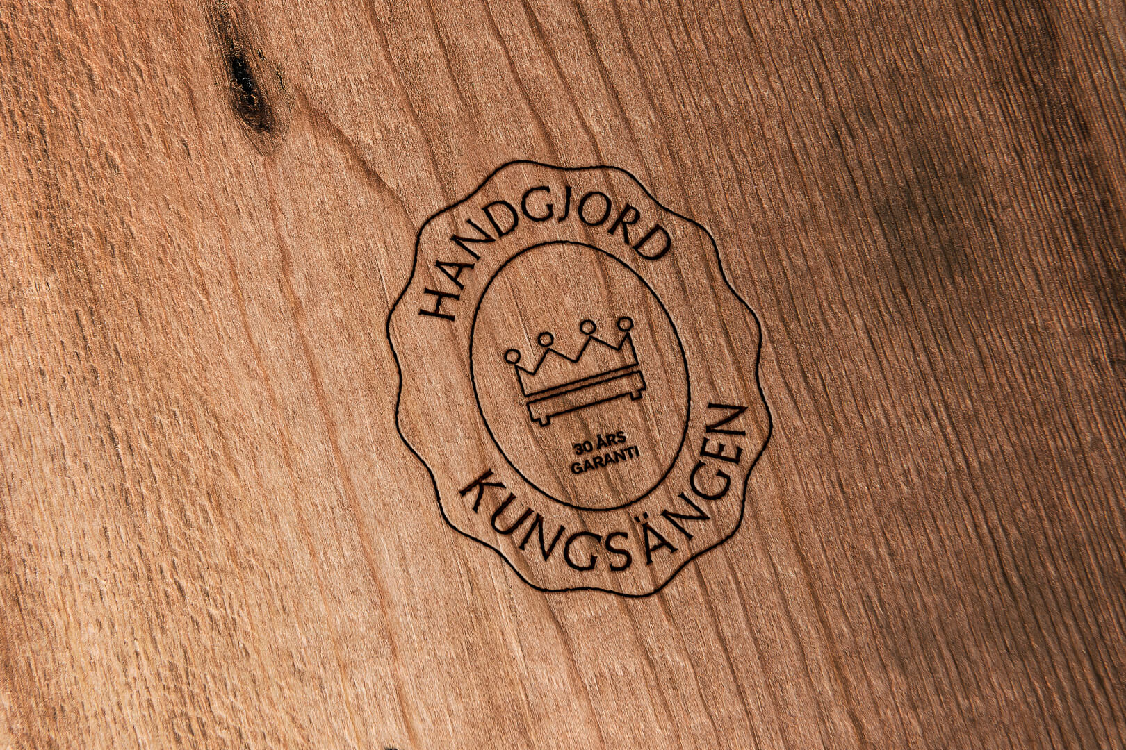 Engraved Kungsängen logo on wood: a crown, a bed, "HANDGJORD KUNGSÄNGEN", and "30 ÅRS GARANTI".