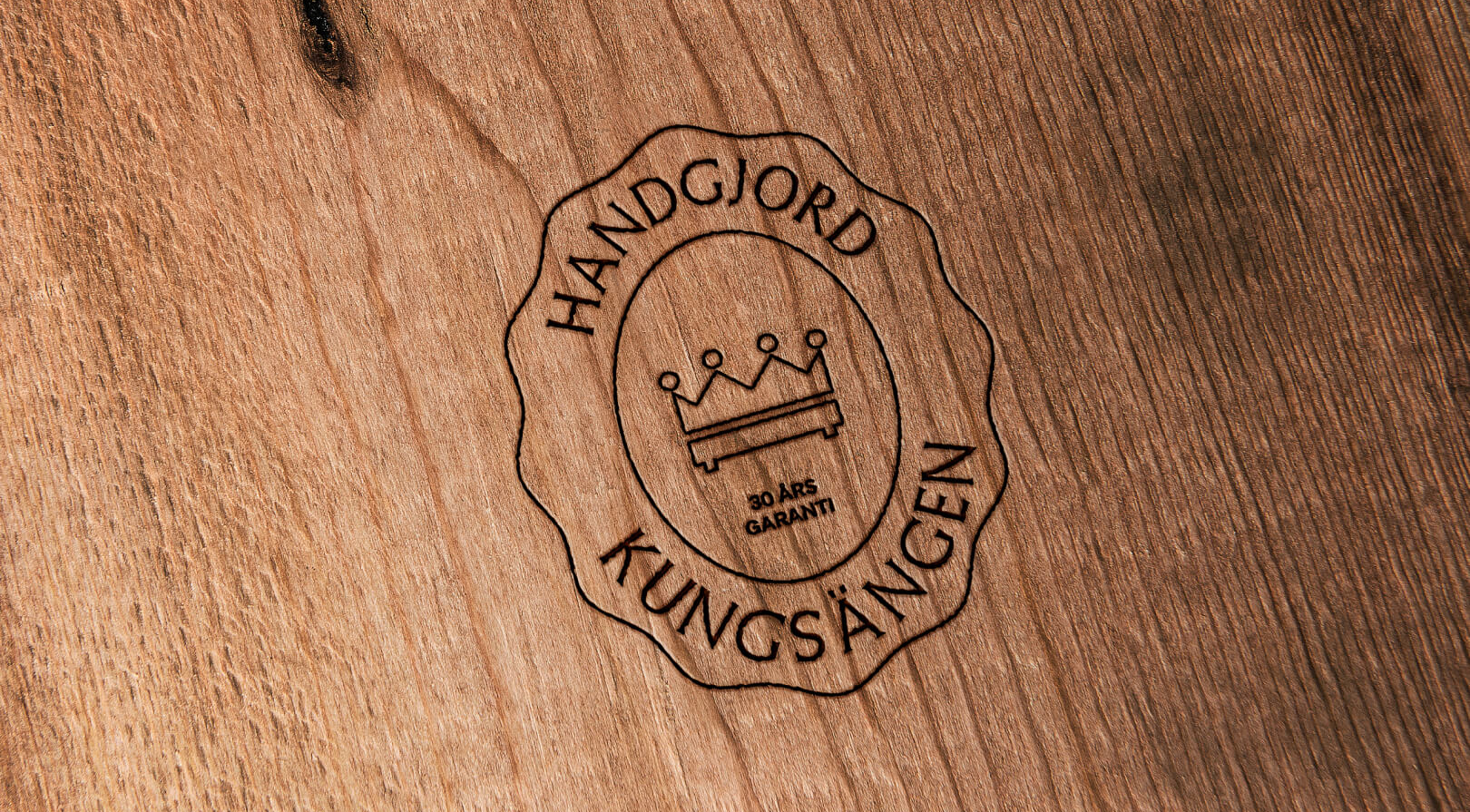 Engraved Kungsängen logo on wood: a crown, a bed, "HANDGJORD KUNGSÄNGEN", and "30 ÅRS GARANTI".