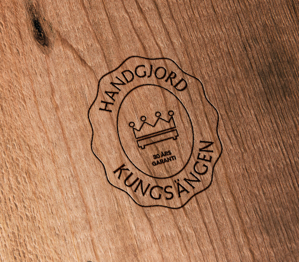 Engraved Kungsängen logo on wood: a crown, a bed, "HANDGJORD KUNGSÄNGEN", and "30 ÅRS GARANTI".