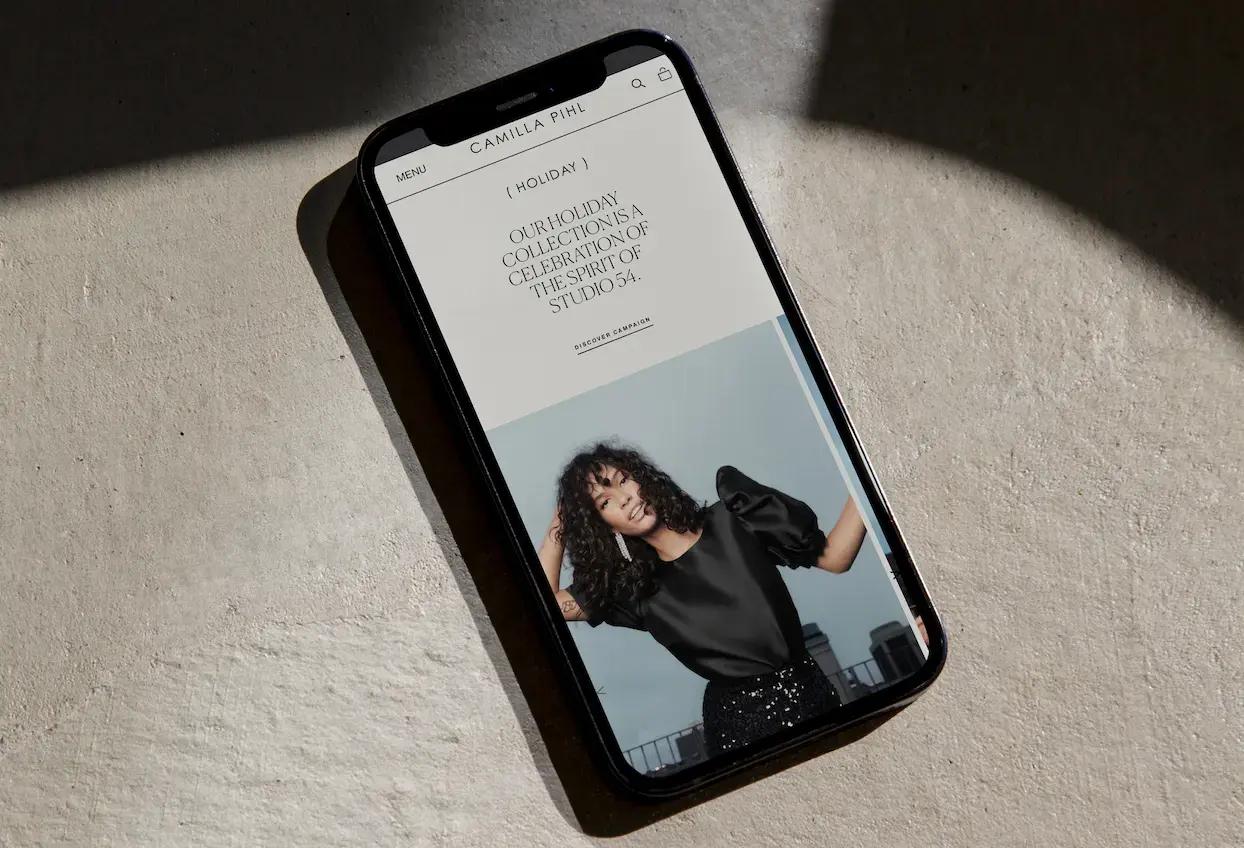 A smartphone displaying a fashion website with a model and text about a "Holiday Collection," resting on a textured surface.