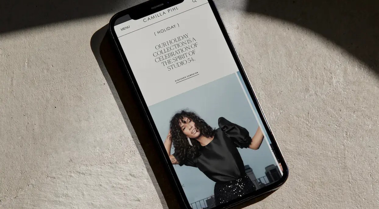 A smartphone displaying a fashion website with a model and text about a "Holiday Collection," resting on a textured surface.
