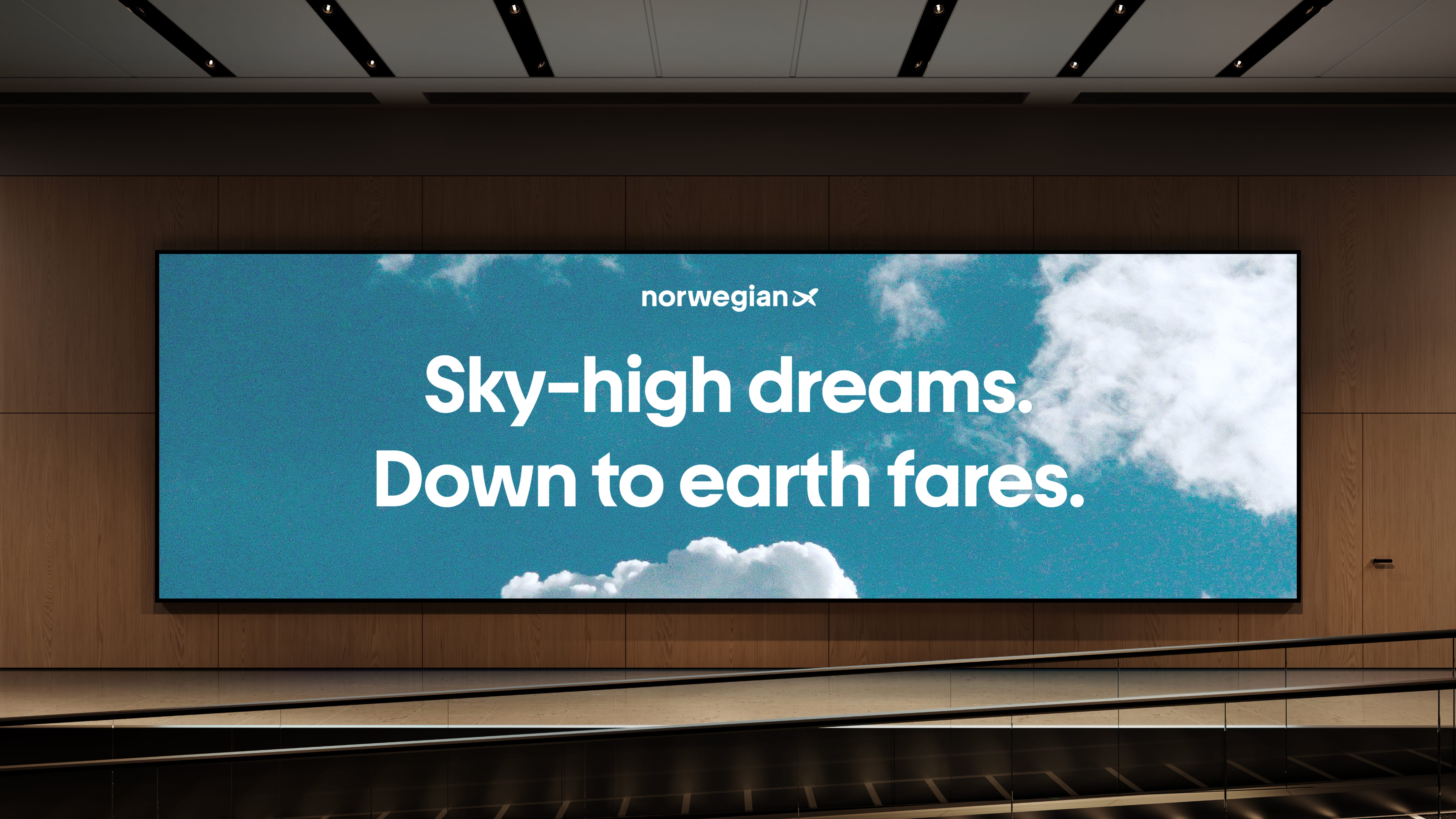 A wide airport screen showing a blue sky with clouds and the text Sky-high dreams. Down to earth fares.