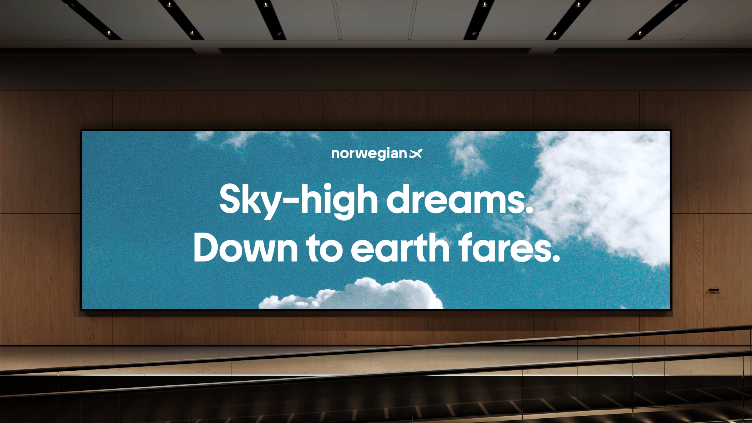 A wide airport screen showing a blue sky with clouds and the text Sky-high dreams. Down to earth fares.