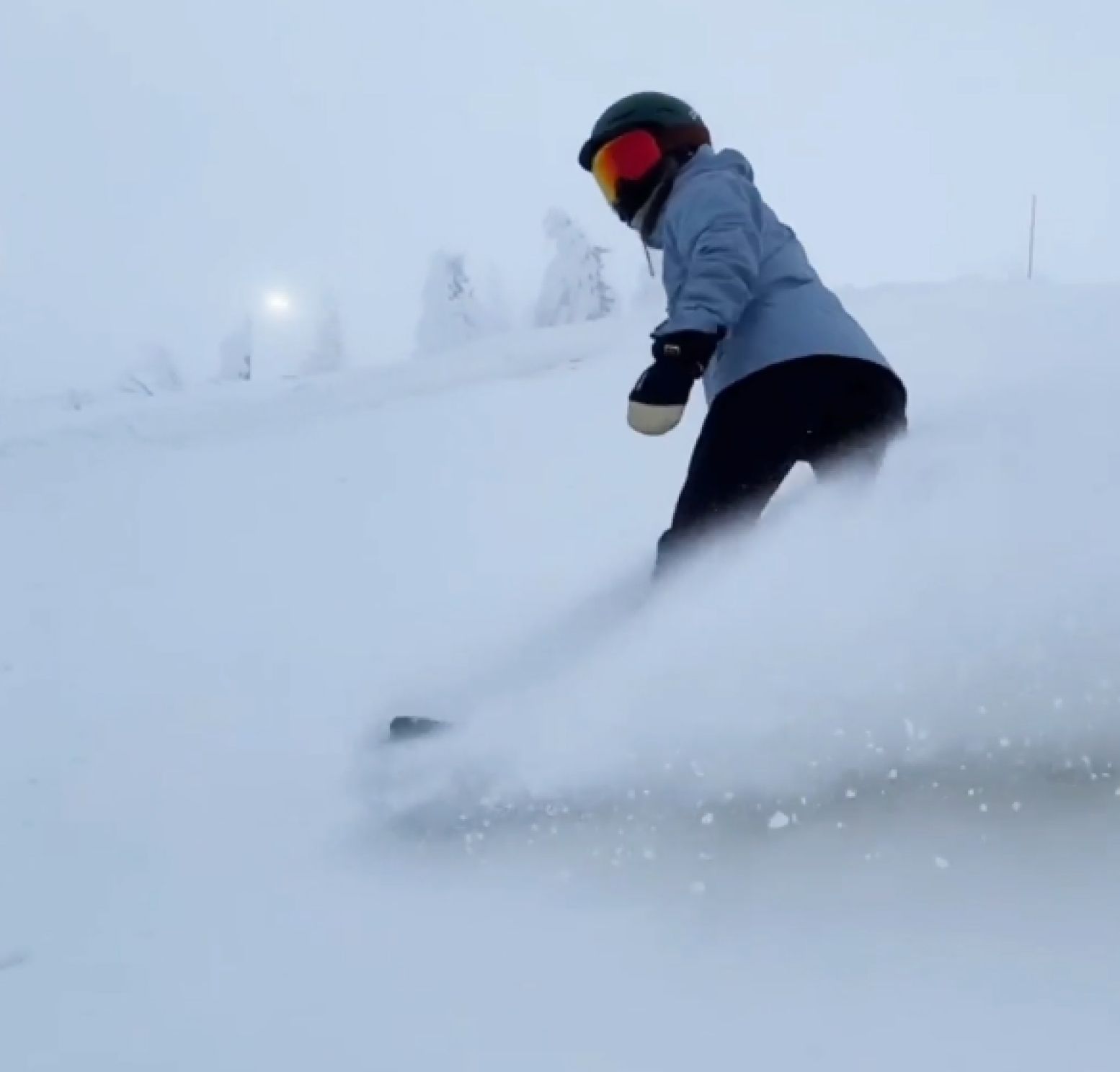 A snowboarder carving through deep powder, spraying snow behind them.