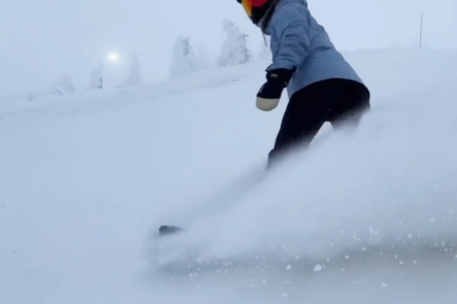 A snowboarder carving through deep powder, spraying snow behind them.