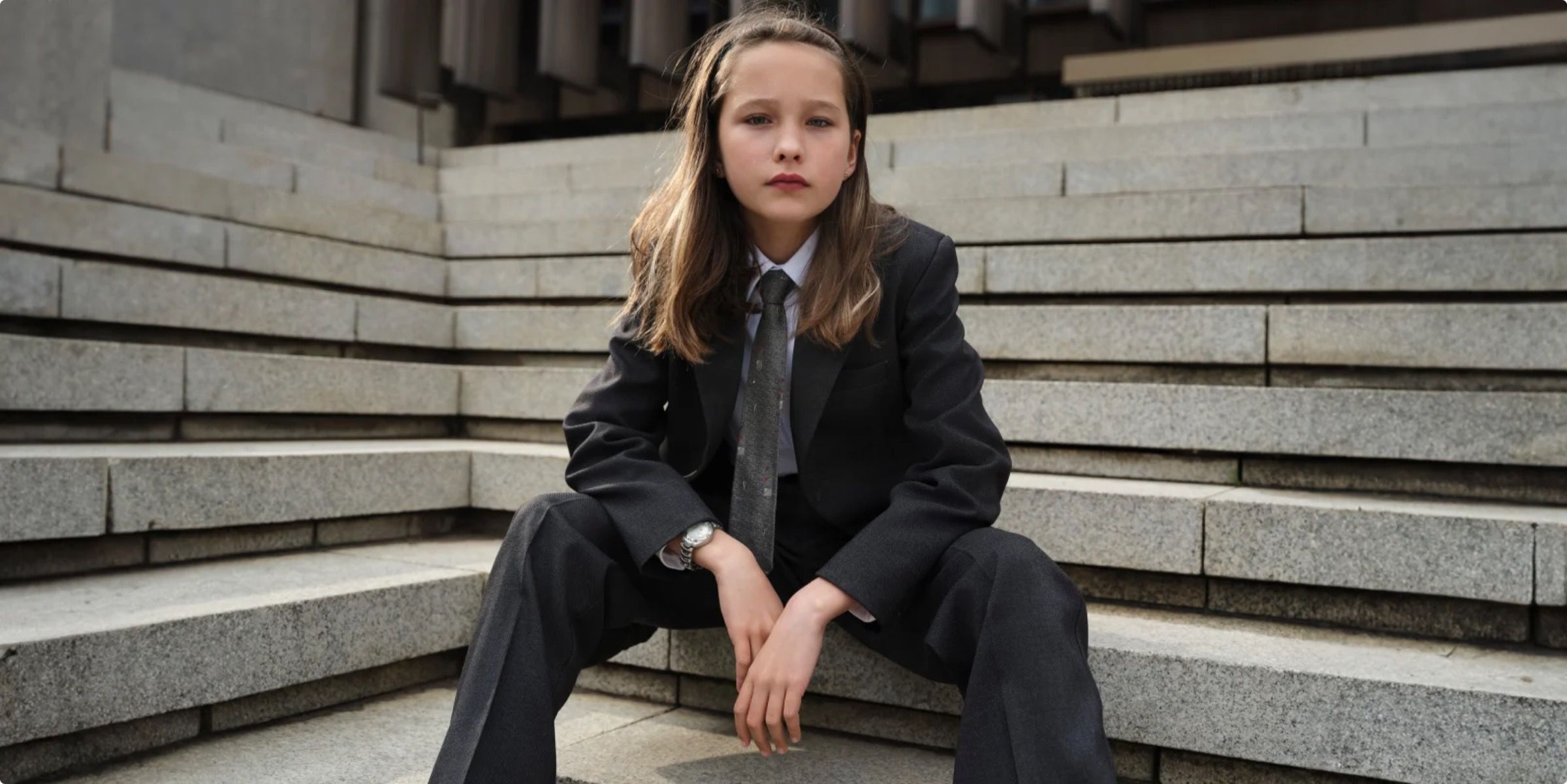 A child in a grey suit sits on stone steps