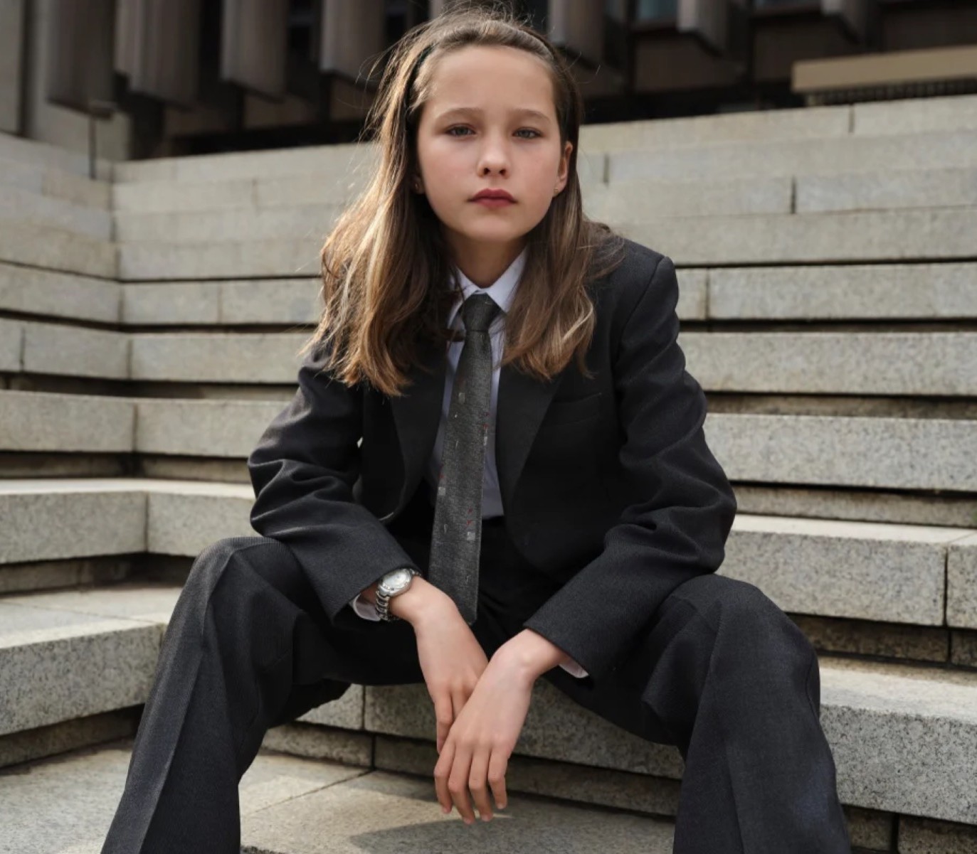 A child in a grey suit sits on stone steps