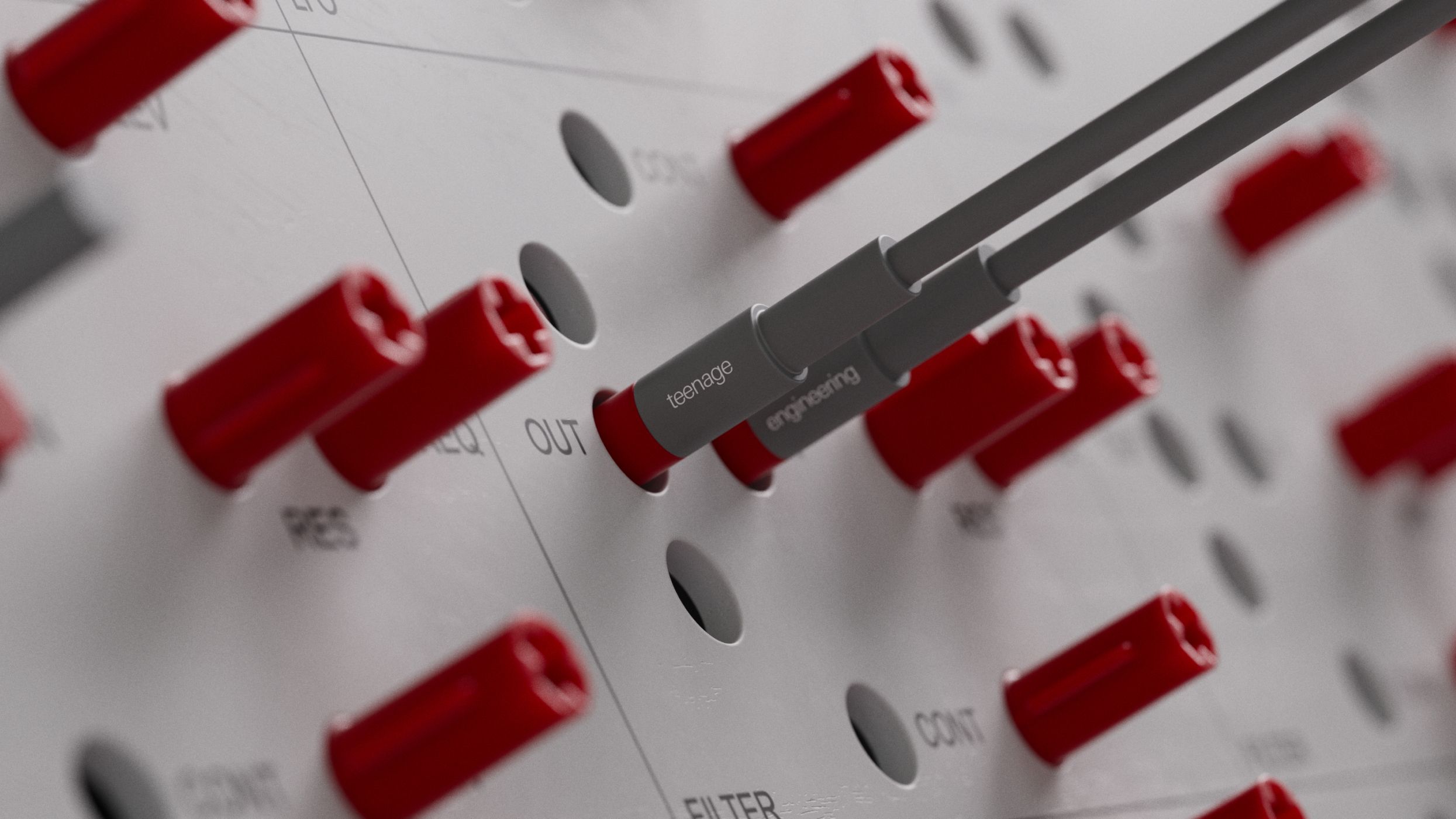 Macro shot of a red patch cable labelled teenage engineering plugged into the drum machine's OUT jack, surrounded by a dense field of red jack sockets.