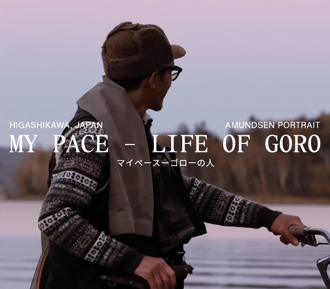 A man in a hat and patterned sweater holds a bicycle by a lake, looking into the distance, with the title "MY PACE - LIFE OF GORO."