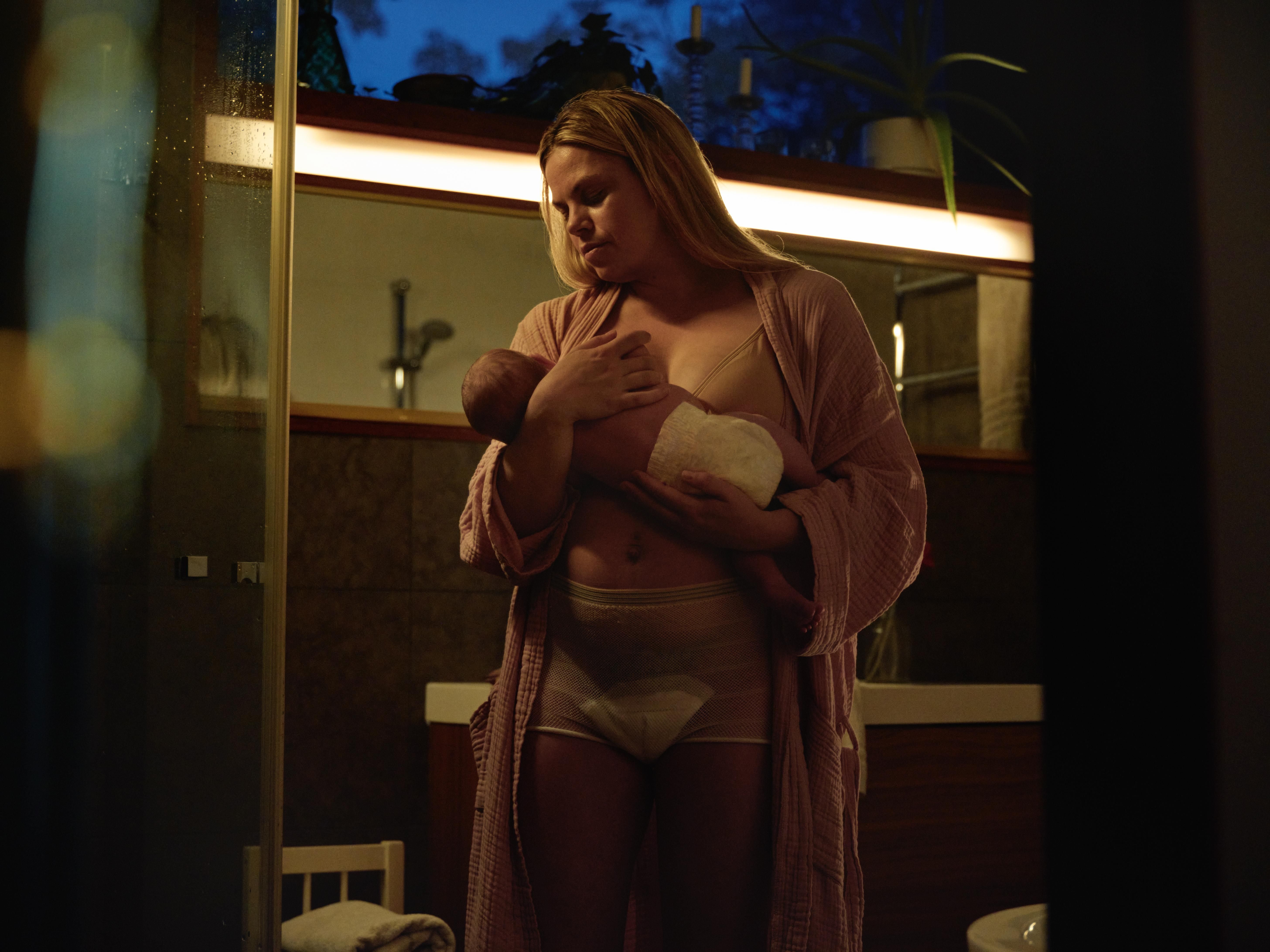 A woman in a robe holds a swaddled newborn in a dimly lit room.