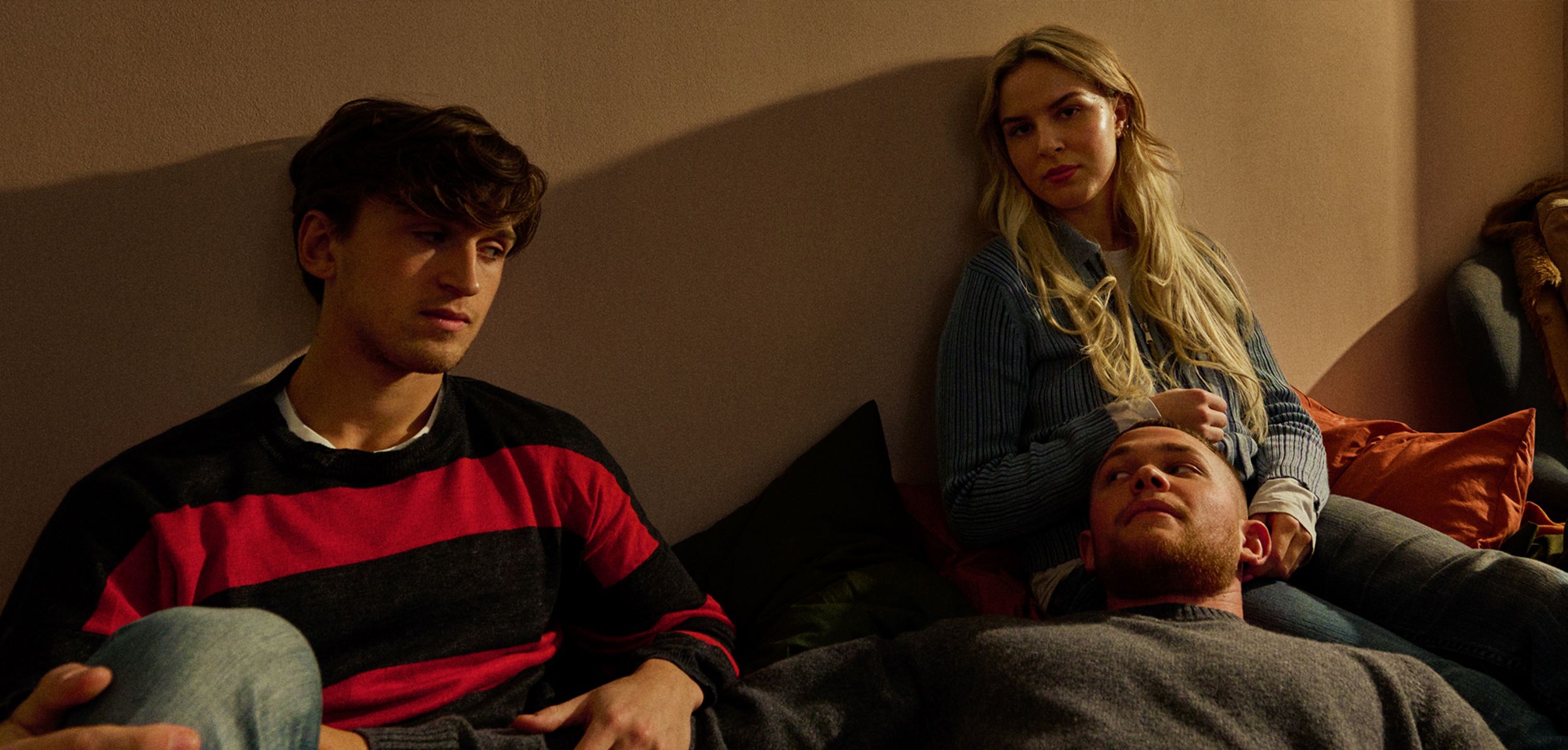 Four friends from Ruset 2's new cast sit together on a sofa in warm evening light, one lying with his head in a woman's lap.