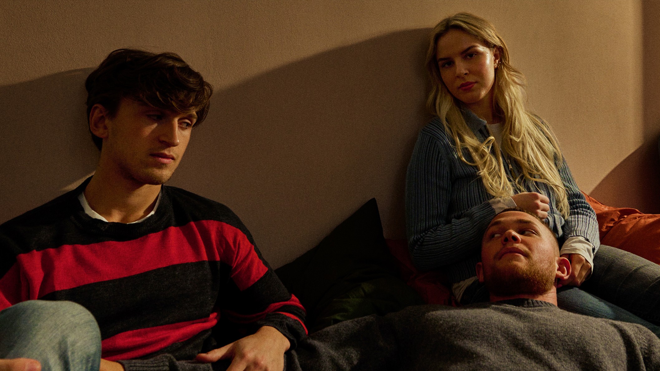 Four friends from Ruset 2's new cast sit together on a sofa in warm evening light, one lying with his head in a woman's lap.
