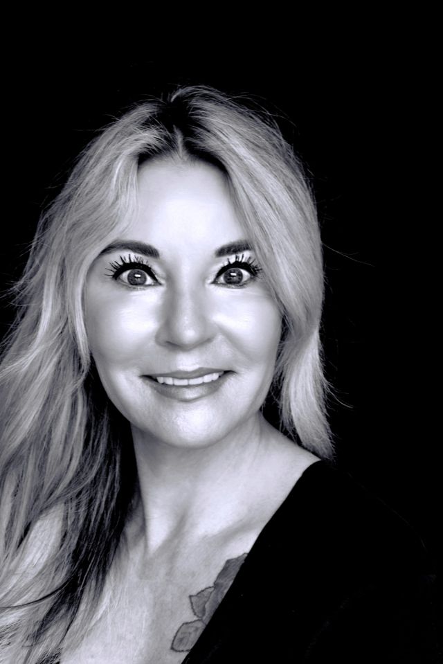 Black-and-white portrait of Linda Harding: a woman with long light-colored hair, smiling gently against a dark background.