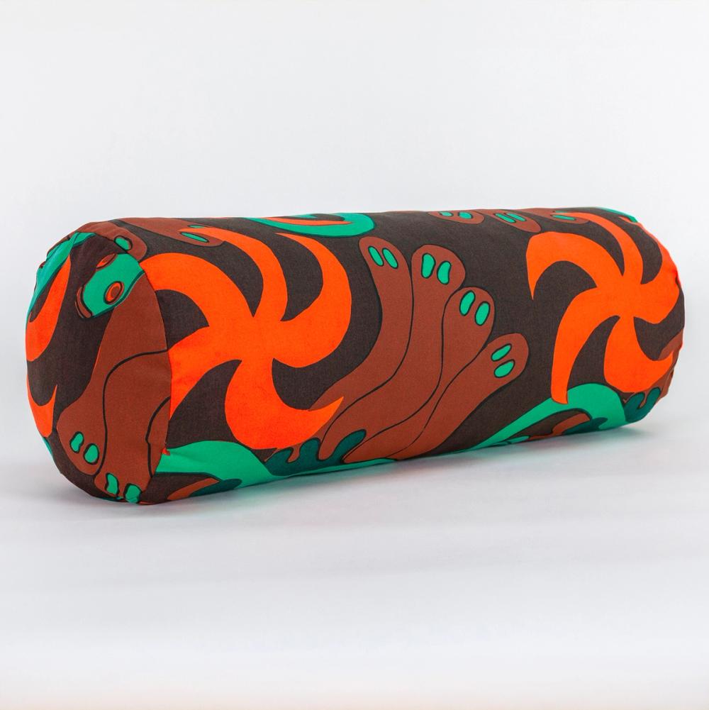 A long cylindrical pillow positioned at a 45-degree angle toward the camera. The fabric making up the pillow features a repeating textile pattern with stylized green snakes intertwined with abstract brown shapes and bright orange spirals on a dark brown background.
