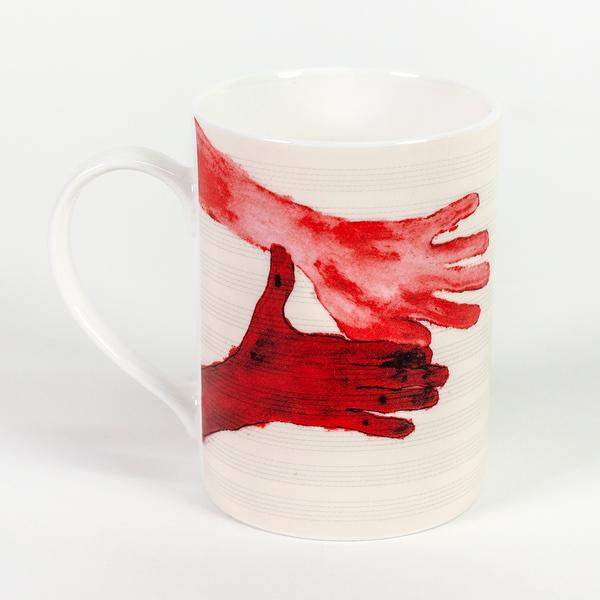 A tall cream colored mug featuring two painted red hands with fingers outstretched in the same direction. The hand on the bottom is darker and points its thumb upward.