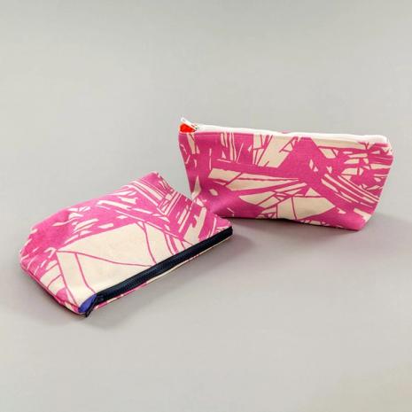 A pair of clutch bags. Wider than they are tall, the bags are composed of hot pink and beige intersecting shapes resembling particle board. Each features a zipper at the top.