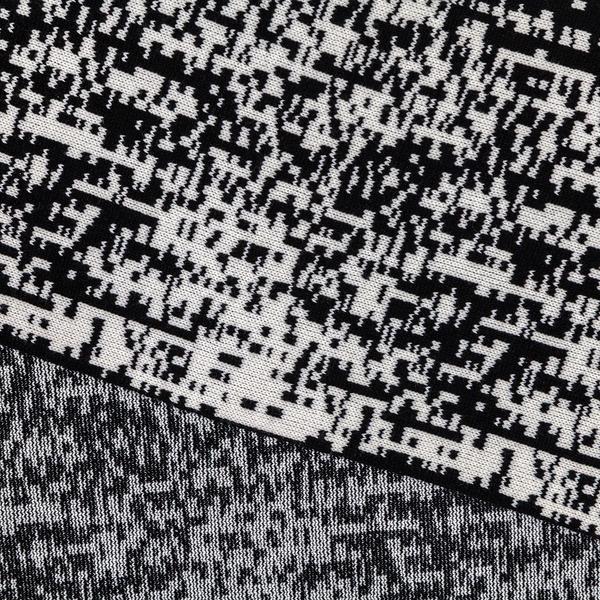 A detail of a scarf with a pixelated black and white pattern, folded over itself so that the underside of the weave is visible.
