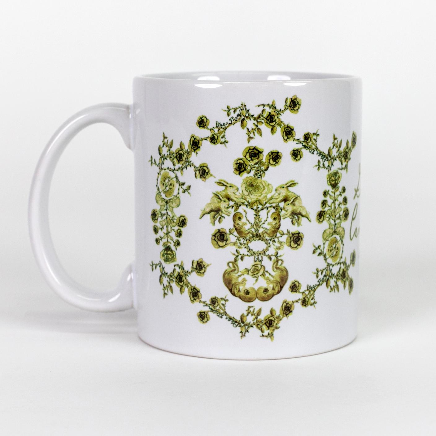 A white ceramic mug featuring a hand illustrated green toile-like pattern made up mostly of roses but also features twin fetuses and rabbits. "you are worthy" is written in green script on the top inside lip of the mug.