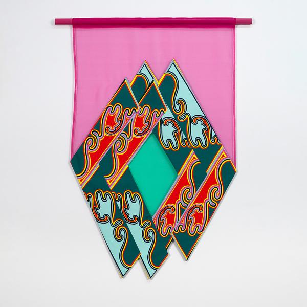 A colorful textile wall hanging with overlapping diamond-shaped panels in a mirrored repeat pattern. Inside there is a sheer green diamond. The overlapping diamonds are framed by a sheer pink fabric background and a pink rod at the top.