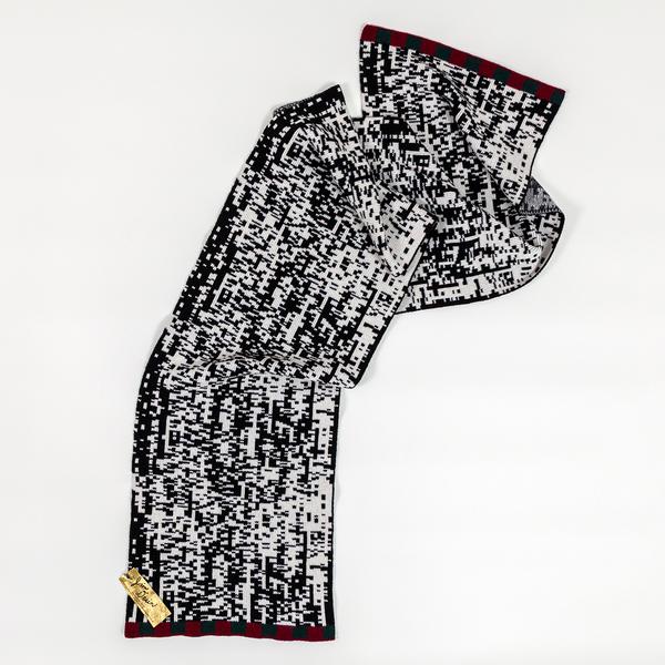 A long scarf with a pixelated black and white pattern. The top of the scarf is draped and bunched while the lower part is stretched flat.