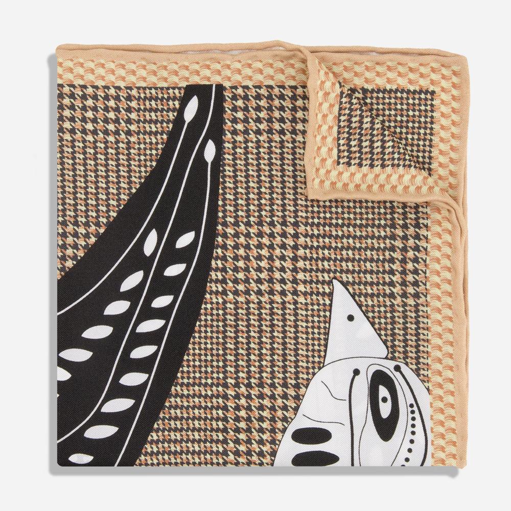 A detail of a folded tan silk pocket square with a woven textured border. There is a glimpse of a printed black and white illustration of sparrow, whose face and beak emerge from the bottom-right corner. Its wing darts across the composition from the bottom-left corner.