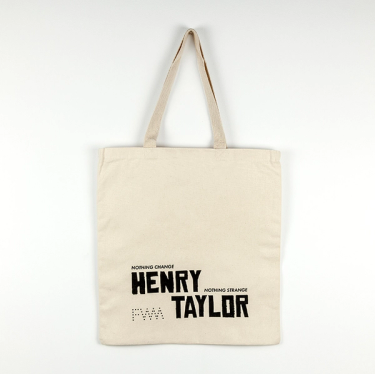 An image of the backside of the cream colored canvas tote bag against a white background. The screenprinting in black says "Nothing Change, Nothing Strange" and the artist's name "Henry Taylor" in large font at the bottom of the tote. In the bottom left corner, is The Fabric Workshop and Museum's logo, "FWM" written in dots.