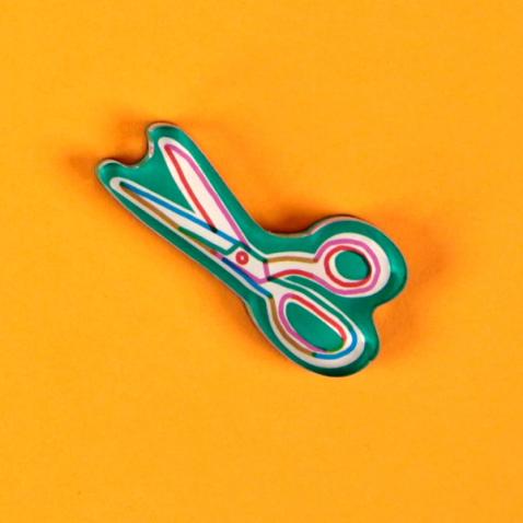 A tool magnet in the form of a green outlined pair of partially opened scissors is laid out against a bright, warm yellow background.