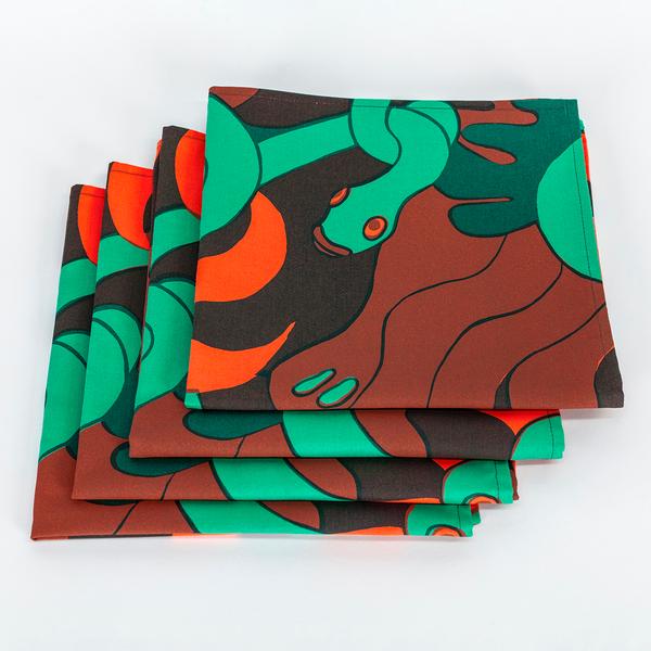 A set of four square napkins made of fabric featuring a repeating textile pattern with stylized green snakes intertwined with abstract brown shapes and bright orange spirals on a dark brown background. The napkins are folded in squares atop one another.