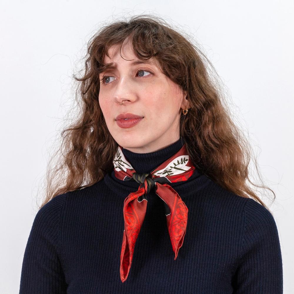 A portrait of a model wearing a red, white, and black silk scarf tied around her neck. The viewer can see there is a floral motif bordering the edge of the scarf.