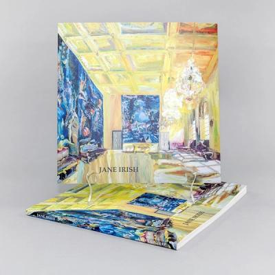 A square book stands upright atop another copy against a gray background. The book cover features a mostly yellow painting of an interior with chandeliers at the right and two blue windows on the left and at the center.