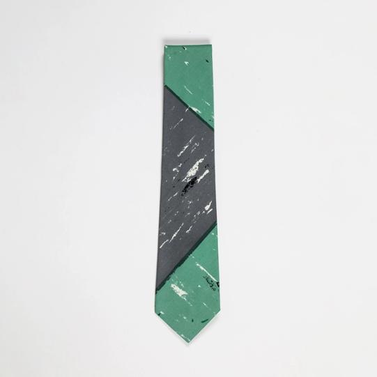A folded necktie featuring a detail of a gray and sea-green checkerboard pattern with scuff marks suggesting a texture like that of linoleum tile.