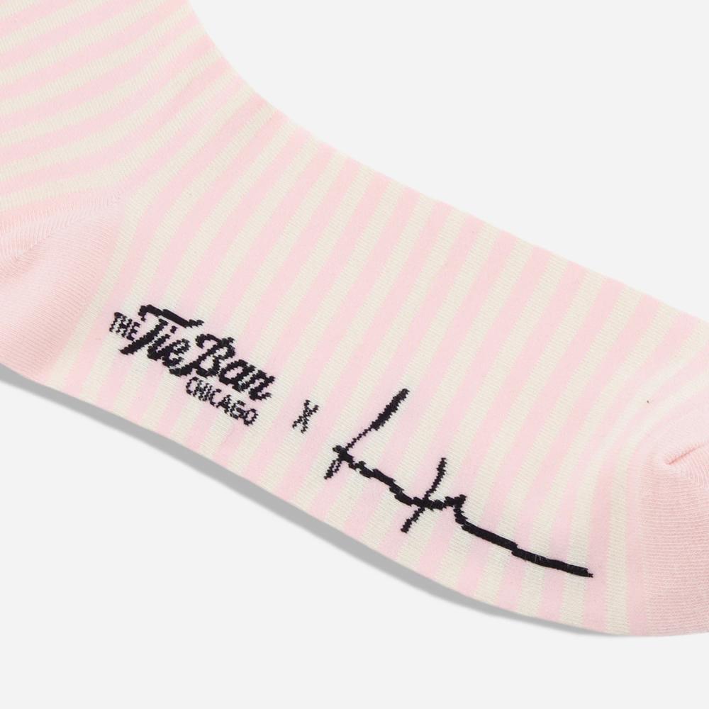 A detail of a light pink and white striped knit dress sock with the artist's signature and "The Tie Bar" logo is featured on the bottom of the sock.